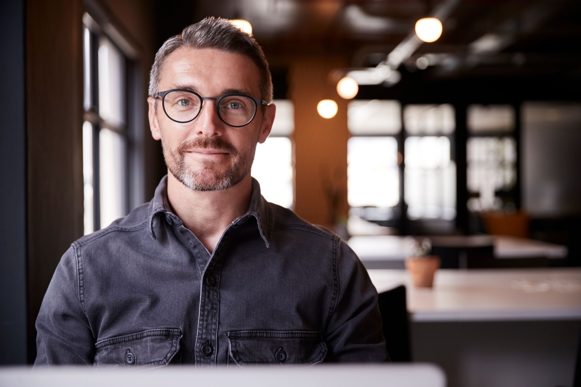 Middle aged white male creative sitting in an office smiling to camera, head and shoulders, close up